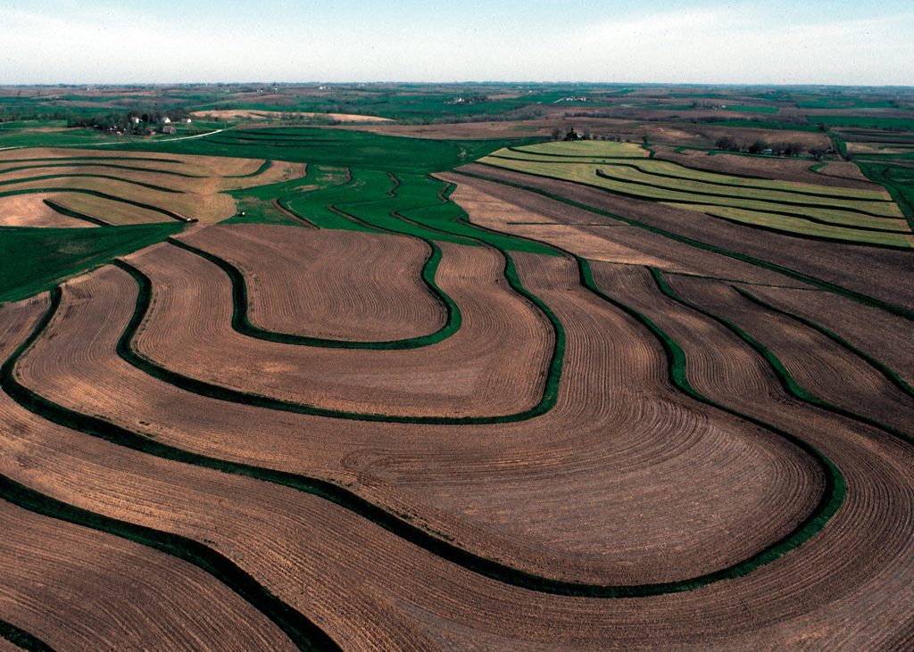 An image taken from an airplane of a terraced field with green, grassed step-back terraces following contours of the field, and brown fields in between the terraces.