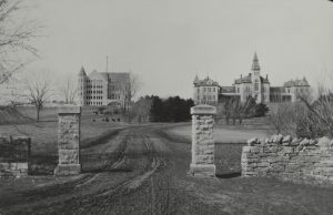 Image of campus from Manhattan Avenue looking west. Anderson Hall and Fairchild Hall are in the distance. Limestone columns and wall are seen in the foreground.