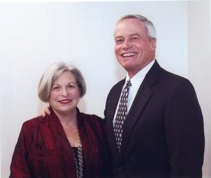 Mary Lee and John Graham smiling standing next to each other, John has his hand on Mary Lee’s shoulder.