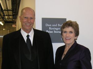 Don and Beth smiling and standing beside the commemorative plaque for the Kesinger Print Storage area.