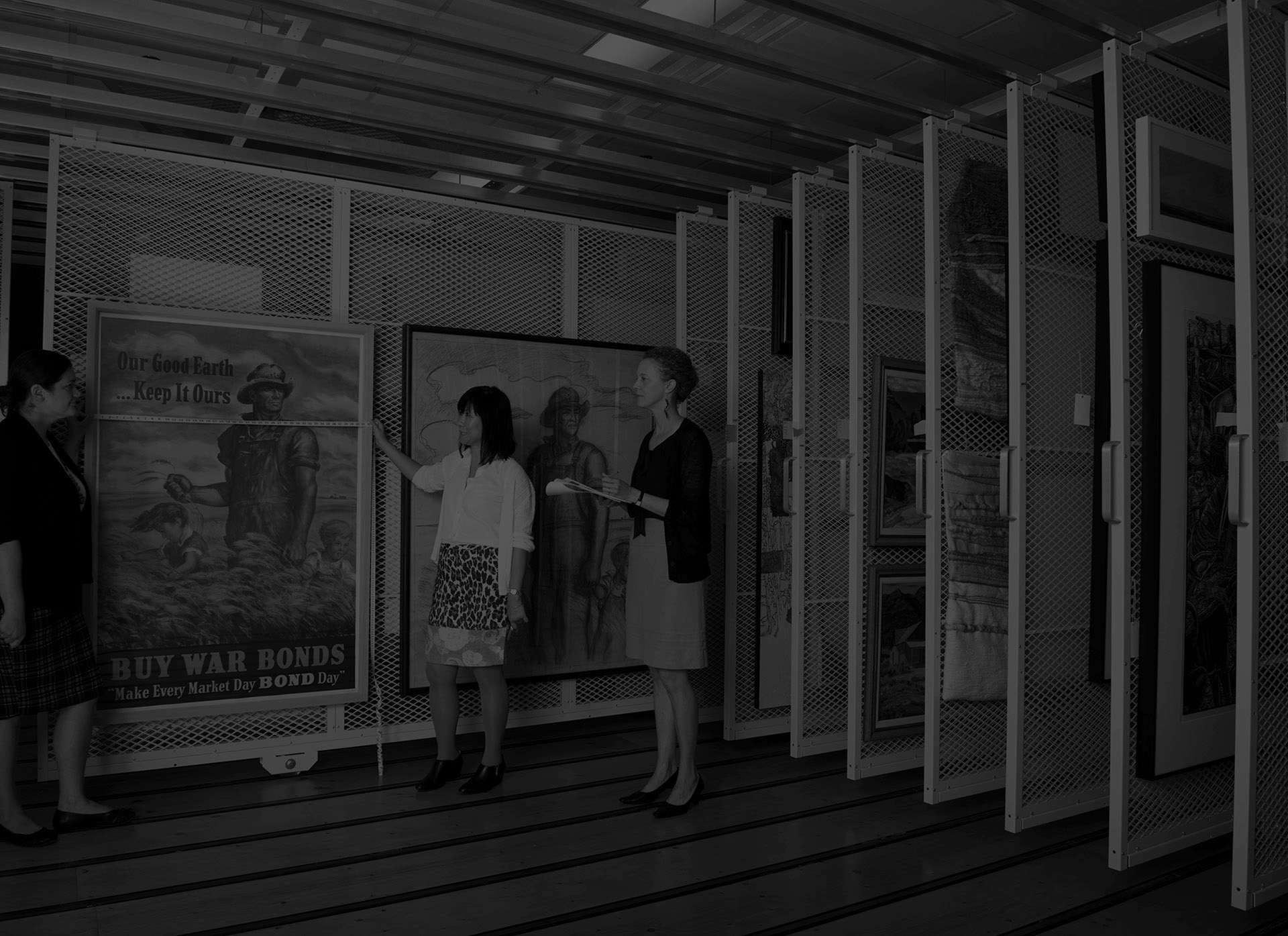 Left to right: Sarah Price, museum registrar, Aileen Wang and Elizabeth Seaton, museum curators, evaluating works of art by John Steuart Curry "Our Good Earth...Keep It Ours, Long May It Wave", War Savings Bond Series E, 1942, and "Study for Our Good Earth", ca. 1942. Photograph taken 2017, KSU Photo Services.
