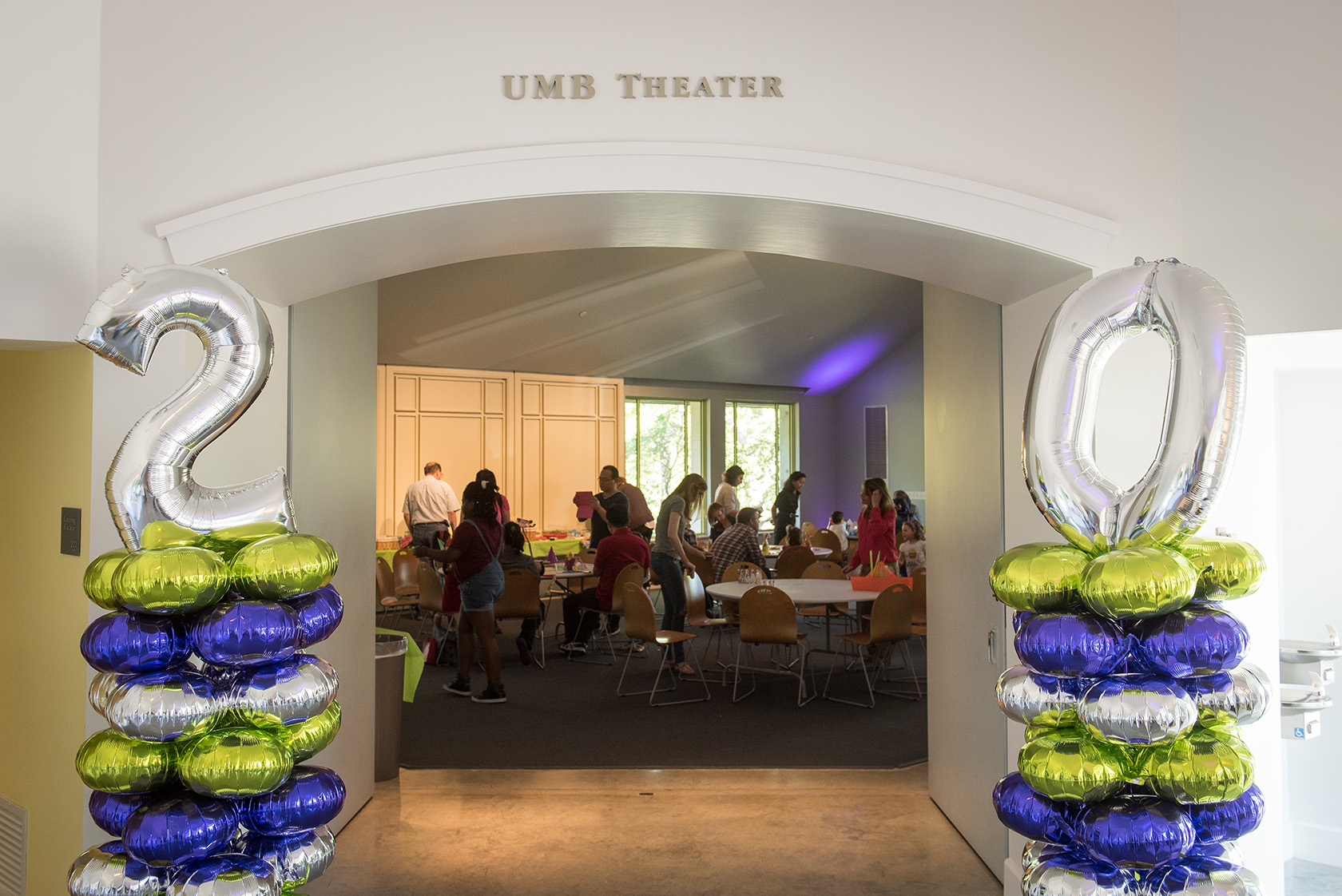 Entrance to the UMB Theater, with people inside setting up for a reception honoring the 20th anniversary of the museum.