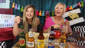 Two women with a line of Mexican beers on the table and a sign that says "Cinco de Drinko"