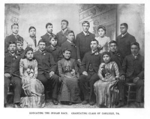 Picture of Native American students dressed in "western" clothes at the Carlisle school. Boys and girls also have hair cut short to look more "American."