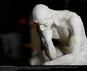 Statue of a man sitting with his elbow on his leg and his hand on his chin - reflecting someone deep in thought.