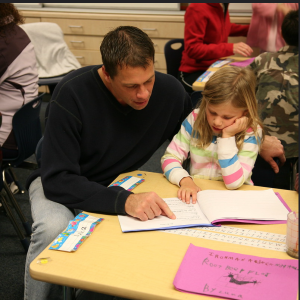 Male teacher pointing at words in a book for a female 2nd grade student.