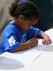 A young, black girl is writing with a pencil.