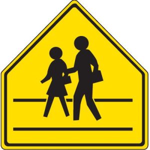 A yellow sign with black border. On the sign are two nondescript almost cartoon people. They're both moving facing toward the left of the sign as if they're walking in that direction. The one in front is smaller and seems to be wearing a skirt and carrying a small black object. The person to the right is taller, seems to be wearing pants, and is also carrying a small black object. His other hand is hanging onto the arm of the person to the left.