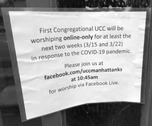 A white paper sign encased in a clear plastic sleeve is taped on a door. The sign reads "First Congregational UCC will be worshipping online-only for at least the next two weeks (3/15 and 3/22) in response to the COVID-19 pandemic. Please join us at facebook.com/uccmanhattanks at 10:45 am for worship via Facebook Live."