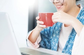 A person sitting in front of a computer holding a red cup