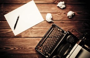 A typewriter, paper and a pen on a table