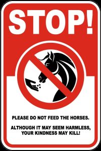 Red sign reads "Stop! Please do not feed the horses. Although it may seem harmless, your kindness may kill!"