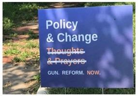 Yard sign from Manhattan, Kansas. It reads, "Policy & Change" and has "Thoughs & Prayers" crossed out. The sign closes with these three words: " Gun. Reform. Now."